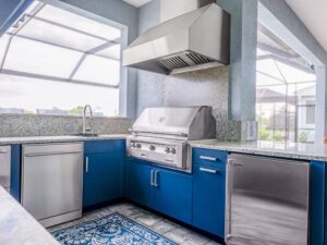 Outdoor kitchen with a stainless steel built-in grill, blue cabinetry, stone countertops, and stainless steel appliances.