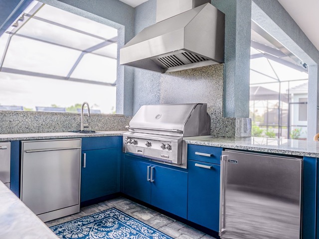 Outdoor kitchen with a stainless steel built-in grill, blue cabinetry, stone countertops, and stainless steel appliances.