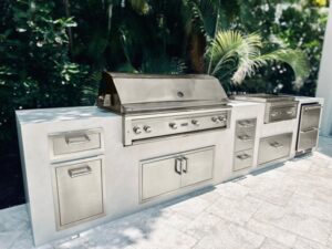 Stainless steel outdoor kitchen with built-in grill, storage cabinets, drawers, and countertop in a tropical outdoor setting.